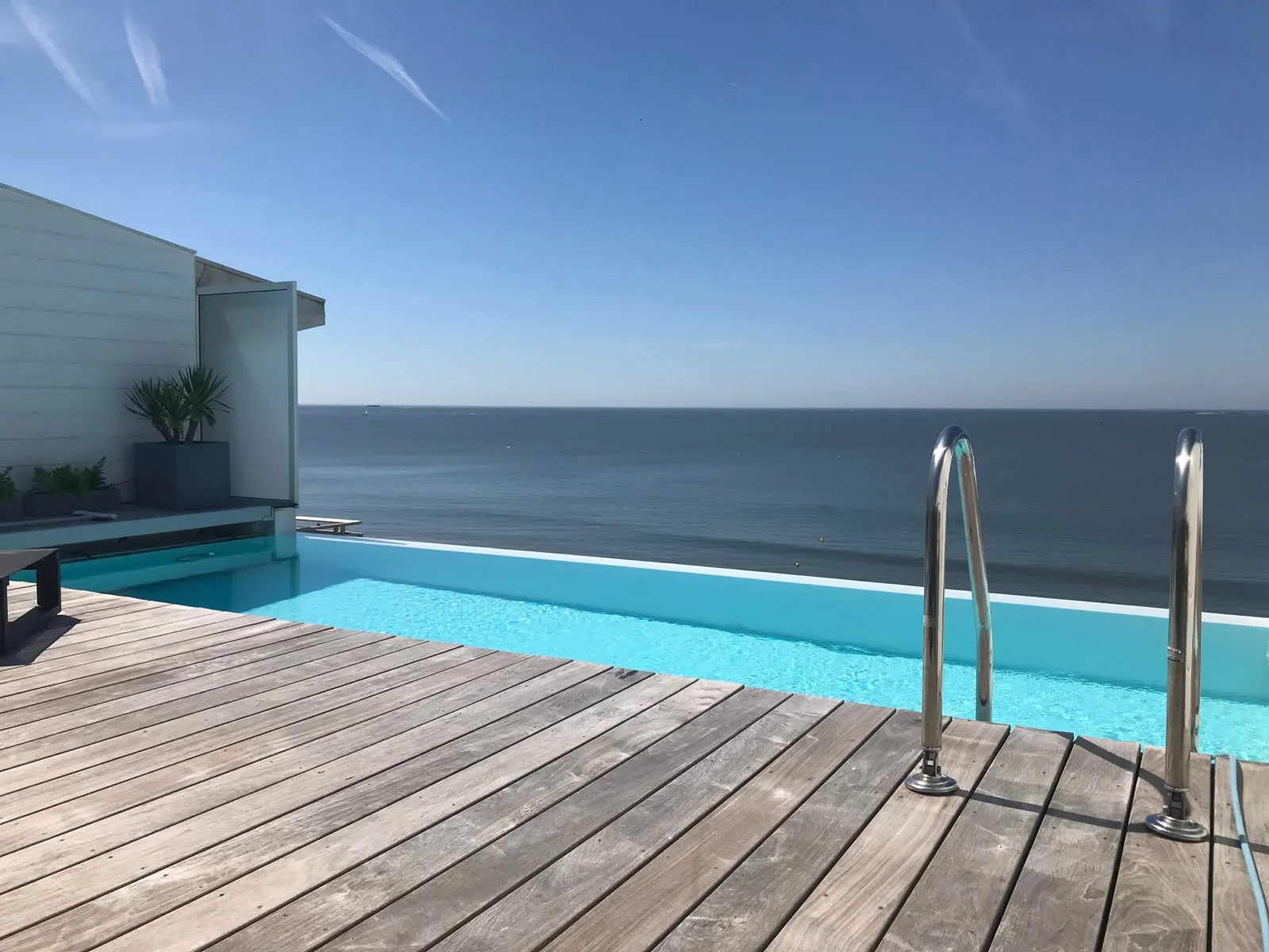 Piscine à débordement réalisée sur le toit d'un immeuble du remblai de La Baule, terrasse en bois et vue sur l'océan.