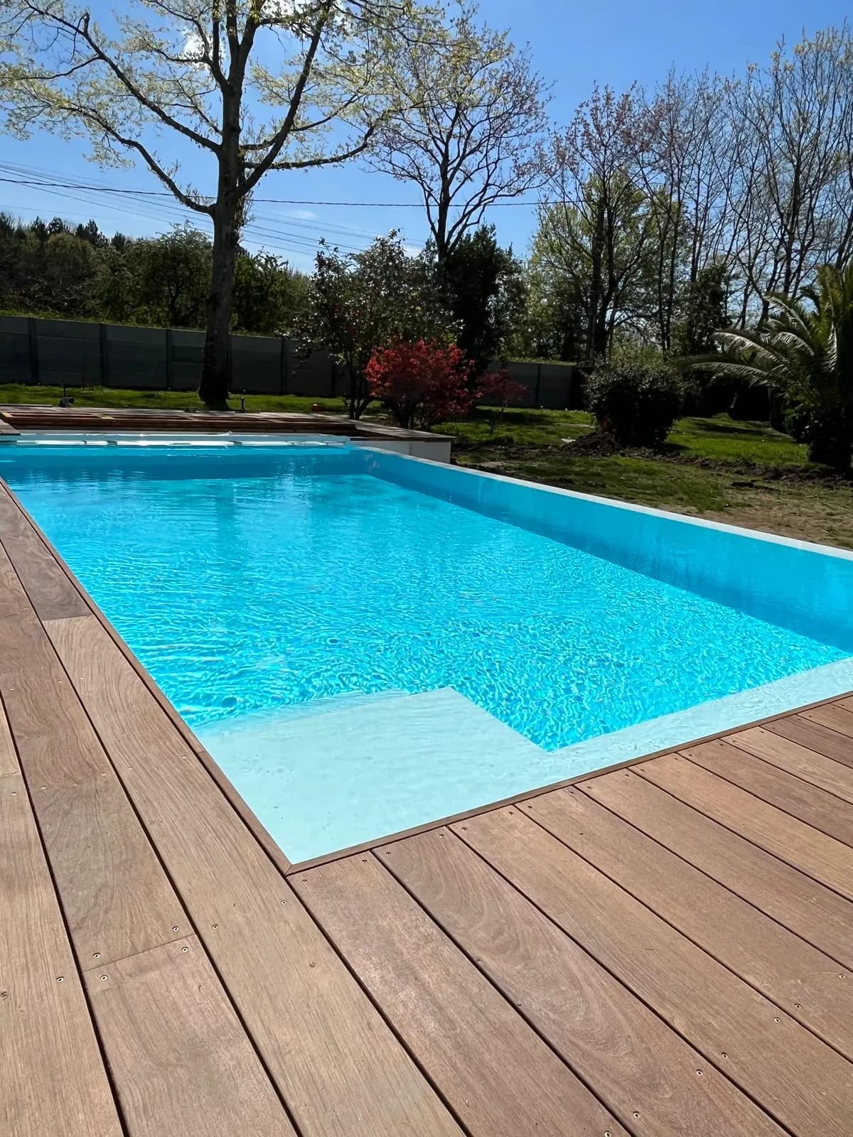 Piscine à liner blanc avec escalier immergé et terrasse en bois, dans un jardin arboré de Loire-Atlantique.