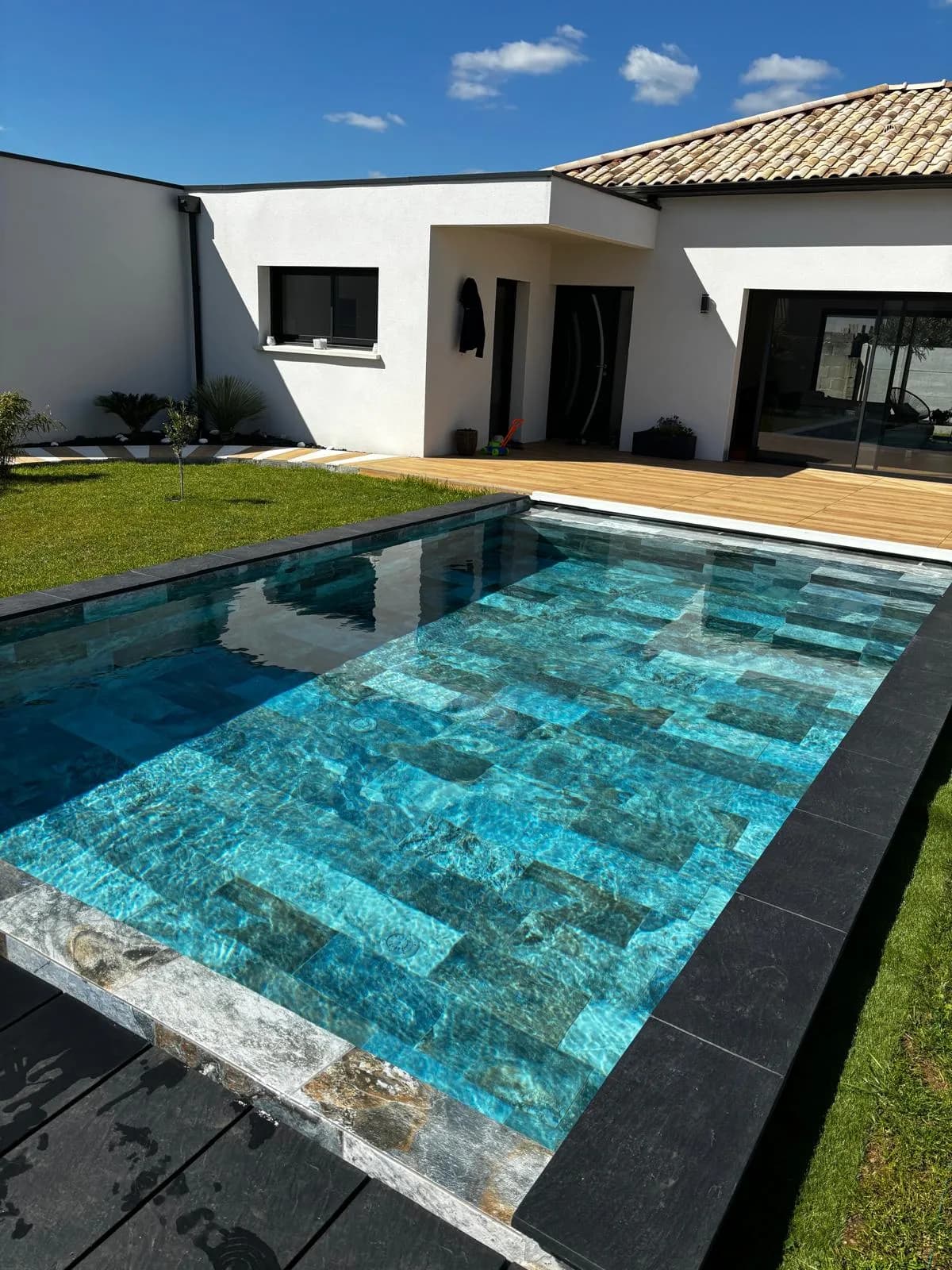Piscine gris anthracite bordée de margelles en ardoise et d'une terrasse en bois composite sombre, eau limpide.